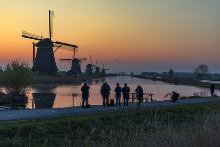 Silhouette of photographers standing and capturing pictures in front the Kinderdijk windmill sunrise during the golden hour, Alblaserdam, Netherlandsの写真素材