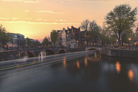 Long exposure boat cruising along the Amsterdam calm canal at the blue sunset hour, Netherlandsの写真素材