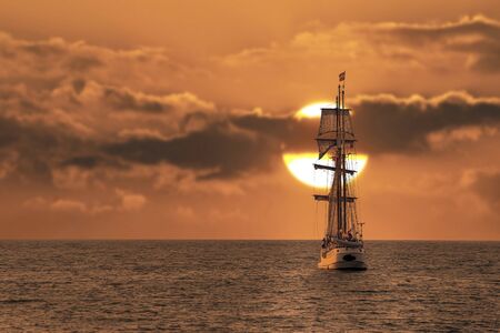 Antique tall ship, vessel leaving the harbor of The Hague, Scheveningen under a warm sunset and golden skyのeditorial素材