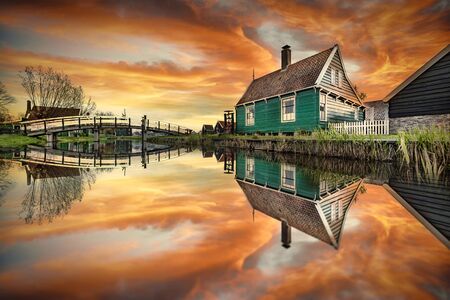 Reflection of the wooden green houses topped with dark orange color roof reflected on the calm water of the canalの写真素材