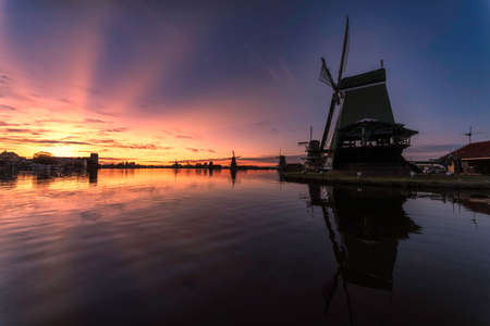 Vivid sunset light beams casts behind the Zaanse Schans city and windmill at the late evening, Netherlandsの写真素材