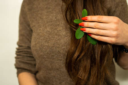 girl with red nails holding a green leaf in her handの写真素材