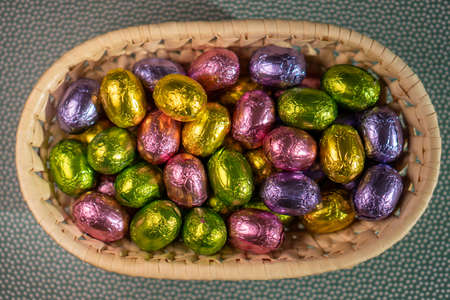 multicolored chocolate easter candies in a basket on a green backgroundの写真素材