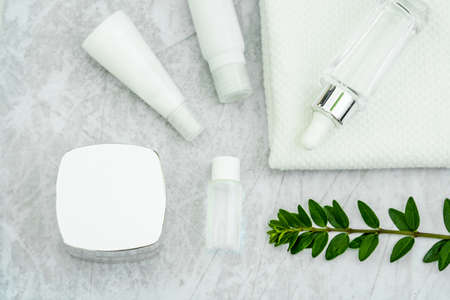 cosmetically flat lay: jars of skin care cosmetics in silver color, white towel and a sprig of luscious greeneryの写真素材