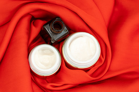 face care creams in gold color on bright red satin fabricの写真素材