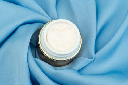 face cream in gold color on bright blue satin fabricの写真素材