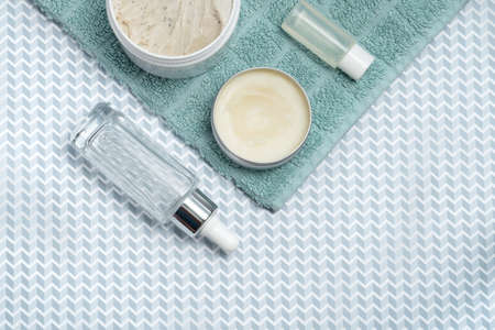 face skin care products. serum, cream, scrub, face tonic, towel and green leaves on a blue backgroundの写真素材