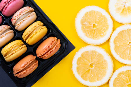 colorful cookies macarons and slices of fresh yellow lemon on yellow background