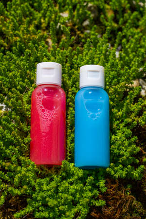 travel size of cosmetics: shampoo and conditioner in red and blue colors laying in gras