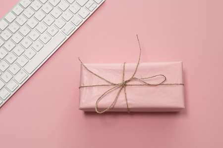 Beauty blog concept. Gift wrapped in a pink paper and modern keyboard on a pink pale background.の写真素材