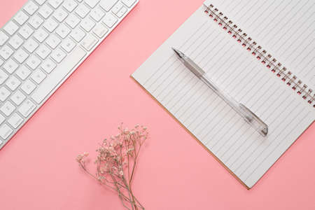 Business concept. Workspace with business accessories: keyboard, pen, notebook and dry flowers on a pink backgroundの写真素材