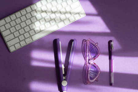 purple flat lay: hair care tool, pen, modern keyboard, sunglasses on a purple background and shadowsの写真素材
