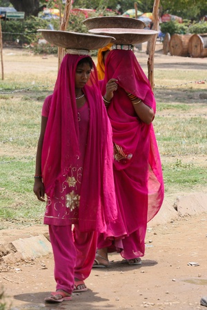 Young indian women in colorful traditional dresses carrying things on their heads in New Delhi, India on a Sunday morning. 27th June, 2010.のeditorial素材