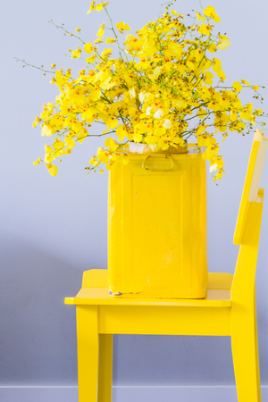 Bouquet of yellow flowers in old metal yellow vase on yellow chairの写真素材