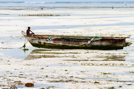 ZANZIBAR, TANZANIA - JANUARY 05: Unknown child on a fishing boat in low tide ocean on Paje beach, Zanzibar, Tanzania on January 5th, 2018のeditorial素材