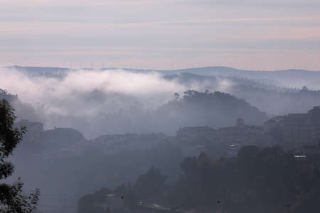 View of Portuguese village, close to Douro Valley through the morning fog, with windmills in the...