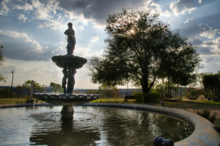 A fountain with a statue of a woman in the middle of it. The water is still and the sky is cloudyの写真素材