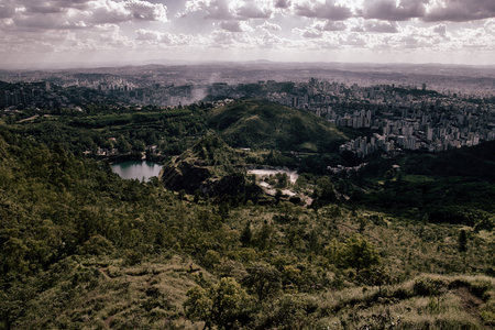 A city with a lake and a hill in the background. The city is surrounded by trees and the hill is covered in grassの写真素材