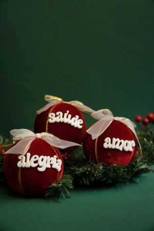 Three red velvet balls with white writing on them. The writing is in Portuguese and says "Health, Joy, Love." The balls are arranged on a green backgroundの写真素材