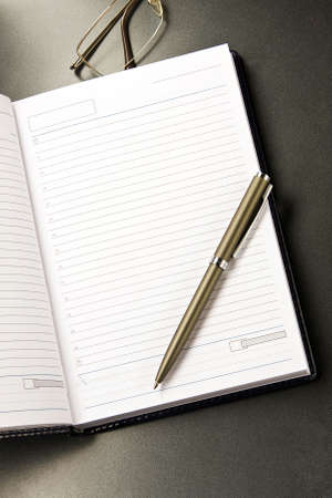 The notebook and glasses with the pen lays on a grey background