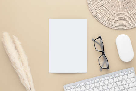 Office desk table top view. Ceramic vase with reed grass and cotton flower, blank paper on Beige table with copy space, Beige workplace composition, flat lay, mockupの写真素材