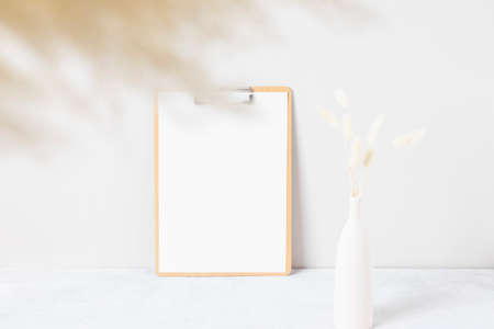 Blank paper card, greeting card mock up. decoration with dried Bunny Tail and pampas grass, Front view, Beautiful Bunny Tail grass in vase and white book on wood table and beige cement wall backgroundの写真素材
