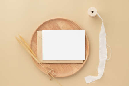 Blank greeting card invitation Mockup on Brown envelope with Dried bunny tails grass on beige background, Minimal table workplace composition, flat lay, mockupの写真素材