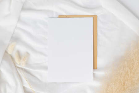 Blank greeting card invitation Mockup on Brown envelope with Dried bunny tails grass on white...