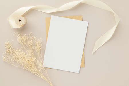 Blank greeting card invitation Mockup 5x7 on Brown envelope with dried flowers on beige background, flat lay, mockupの写真素材