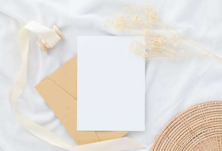 Blank greeting card invitation Mockup 5x7 on envelope with dry flowers and ribbon on white fabric background, flat lay, mockupの写真素材