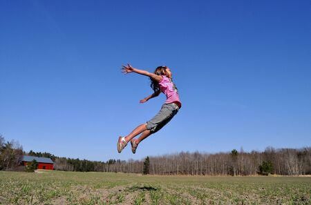 A young girl jumps in the countryside, happy that the spring finally has arrived.の写真素材