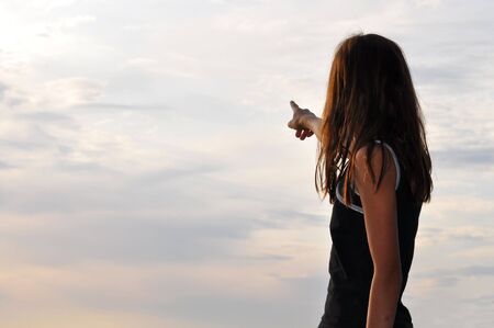 A young girl pointing out at the clouded sky.の写真素材
