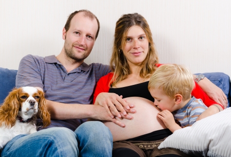 Happy young family sitting on the blue sofa expecting new babyのeditorial素材