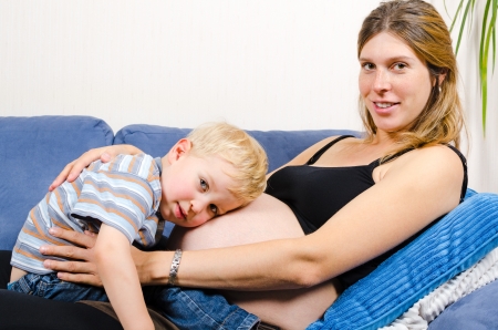 Smiling pregnant mother with her cute little boy on the sofaのeditorial素材