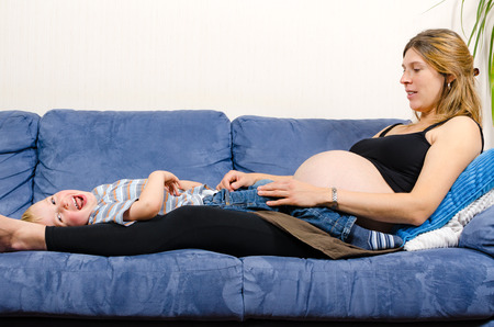 Smiling pregnant mother with her cute little boy on the sofaのeditorial素材