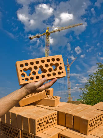 pallet of lightweight bricks. In the palm of your hand is a brick. Against the background of the two tower cranes.の写真素材