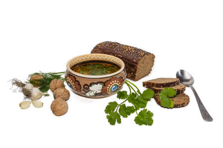 Ceramic bowl of soup, bread, spoon and some of the ingredients for cooking - walnuts, garlic, dill, coriander leaves on a white background. Isolation.の写真素材