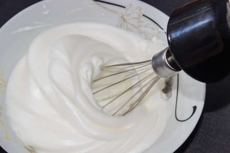 Process of whipping egg whites with a mixer. Working mixer and bowl with whipped whites on a dark background.の写真素材
