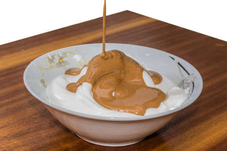 Bowl with whipped egg whites, poured cream with cocoa, on a wooden surfaceの写真素材