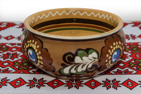 Glazed ceramic bowl with floral ornaments on the tablecloth with a white background.の写真素材