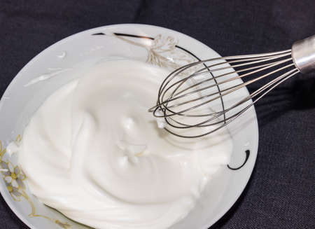 Whipped egg whites in a bowl and whisk from the mixer on a dark backgroundの写真素材