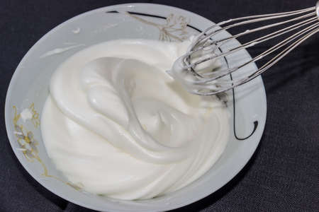 Whipped egg whites in a bowl and whisk from the mixer on a dark backgroundの写真素材
