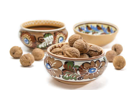 Ceramic bowl with floral ornaments with walnuts on a background of other dishes and nuts on a light background. Isolation.の写真素材