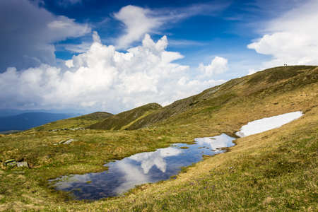Cumulus cloud over the mountain ridge reflected in a small lake.の写真素材