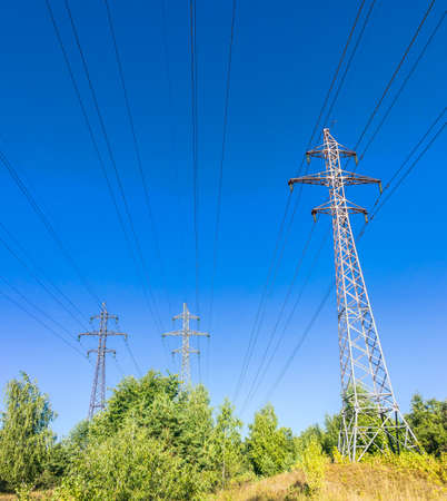 High-voltage power line with the poles, insulators and wires on a background of trees and skyの写真素材