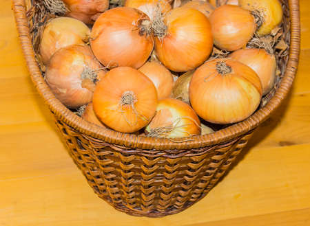 Fragment of a basket filled with ripe onion on the background of the wooden floorの写真素材