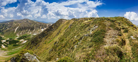 View along the ridge with grassy slopes, snowfields and rocky outcrops on the background of the sky with cumulus clouds. Panorama, Carpathians.の写真素材