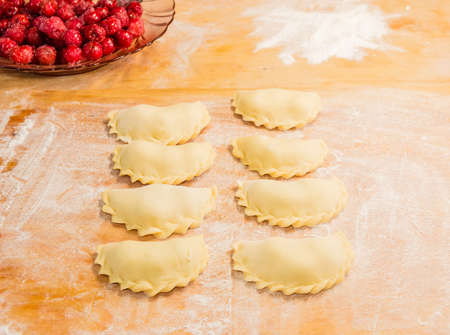 Making ukrainian varenyky (dumplings) filled with sour cherry with sugar on a wood cutting boardの写真素材