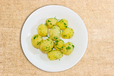 White dish with boiled young potatoes with butter, sprinkle with chopped dill on the surface of scrim.の写真素材