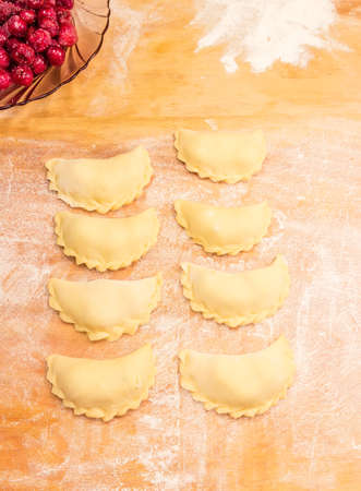 Making ukrainian varenyky (dumplings) filled with sour cherry with sugar on a wood cutting boardの写真素材